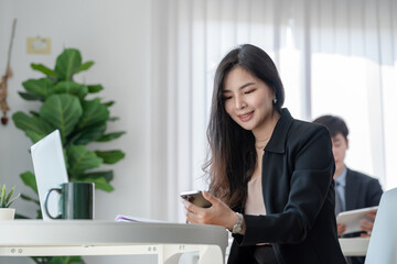 Beautiful Asian businesswoman sitting in the office holding a smartphone.