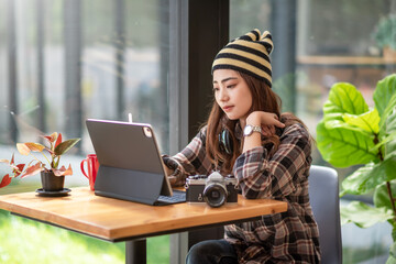 Image of a Asian woman wearing headphone using tablet and camera on table.