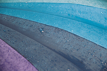 Wet waterproof textile surface of blue turquoise color umbrella under drizzle rain. Water drops dripping at grey blue umbrella fabric texture. Rainy weather abstract background