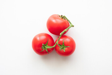 Three red tomatoes connected by a green branch. View from above