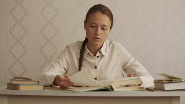 Young woman student sits at the desk, turning pages of old torn book, looking for table of contents and right chapter. Education concept, studying at home, library, prepare for exam, doing homework 4K