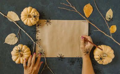 Halloween grunge black background, pumpkins, black spiders, dry branches, orange leaves decoration. Autumn composition frame, flat lay, vintage paper, woman hand with pencil, copy space.