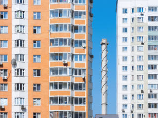 Fototapeta premium Chimney tube against a blue sky surrounded by apartment buildings