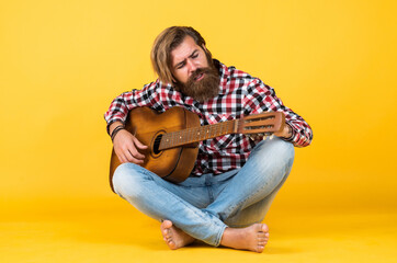 favorite tune. Portrait of happy bearded male playing guitar. a lonely musician. cheerful handsome mature man playing guitar and smiling while sitting on yellow background