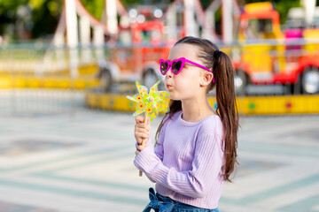 a child girl in an amusement park in the summer blows on a toy spinner near the carousels in...