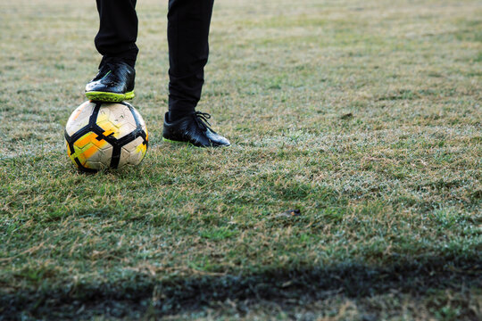 Lower body extremity shot of a man standing on the field stepping on a soccer ball with one foot