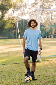 full body shot of a man with curly hair stepping over a soccer ball with one foot on a field