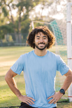 Half Body Shot Of A Man With Curly Hair Smiling With Arms On His Hips Standing On A Soccer Field