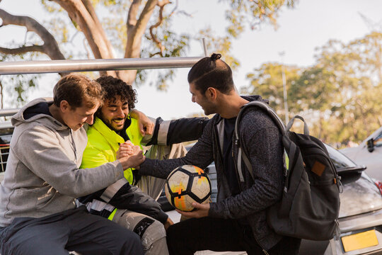 horizontal shot of men with one holding a soccer ball and two shaking hands all in casual clothes