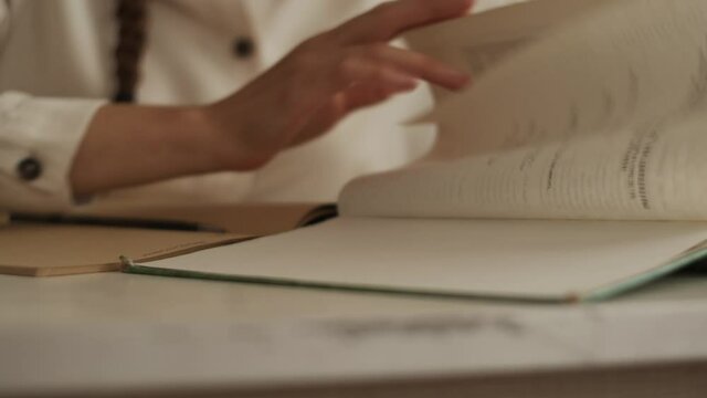 Close up view of female student sits at the desk, watch table of contents in old torn book, look for right chapter, flipping pages. Education concept, study at home library, prepare for exam, homework