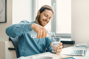 Young happy businessman pouring water into glass, smiling while taking break and reducing thirst,...