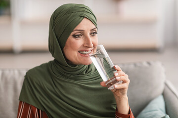 Cheerful Senior Muslim Lady In Hijab Drinking Water At Home