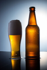 brown bottle of beer poured into a glass of foamy beer, on a water background