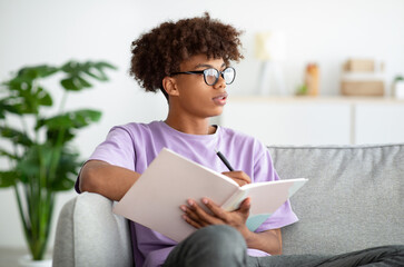 Serious black youth studying with notebook, writing down info, getting ready for exam or test at...