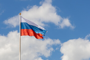Flag of the Russian Federation on a pole against the sky with clouds, frontal view. The flag of Russia waving in the wind on a sunny day. Flutters Russian tricolor. Copy space, place for text