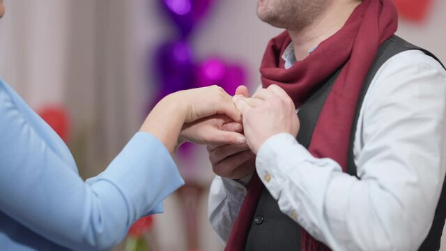 Close-up side view of loving husband boyfriend kissing hand of unrecognizable wife girlfriend smiling. Happy thrilled Caucasian man expressing feelings to woman on Valentine's Day