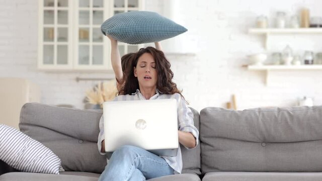 Work from home with naughty kid: young mother businesswoman try to concentrate on business email in laptop with distracting little son hitting mom with pillow. Disobedient boy disturb freelancer mom
