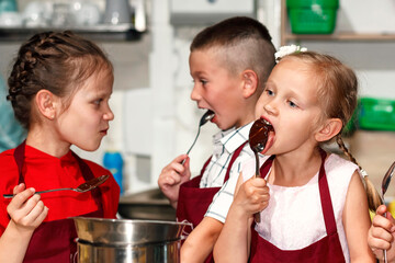 Children Cook Chocolate in kitchen aprons. Little girl and boy lick spoons of chocolate