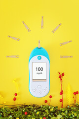 A blood glucose meter with test strips in the form of sunlight on a yellow background with flowers. The concept of life without diabetes, health with glycemic control and a good blood sugar levels