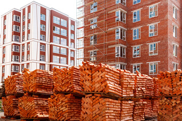 Pallets with bricks on a background of brick high-rise buildings. Construction site with scaffolding near the house