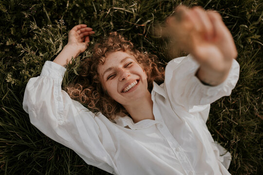 young happy, smiling woman with curls is lying in the grass enjoying spring
