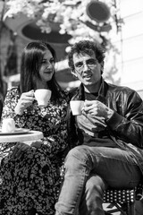 A young married couple is having breakfast in restaurant on terrace. A man and a woman drink coffee and communicate.