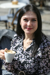 Smiling stylish woman in black shirt sitting at the table drinking coffee in the terrace of restaurant.