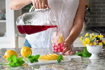 Woman is pouring colorful red cold summer drink into a glass with ice