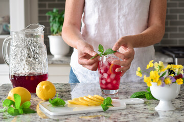 Woman is garnishing colorful red cold summer drink with mint leaves