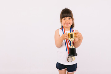 Little brown-haired girl with sports champion medals, holding a trophy with both hands. Sport and victory concept