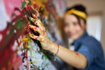 Female painter applying paint on canvas with fingers while creating a large modern abstract oil...