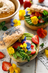 Bagel sandwich with addition avocado slices and edible pansy flowers, close up view. Delicious and beautiful vegan food