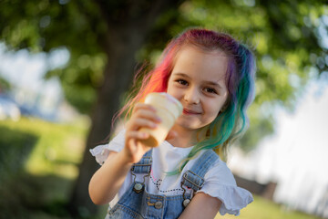 Happy little girl with colorful dyed hair eating ice cream outdoors in park. Image with selective focus