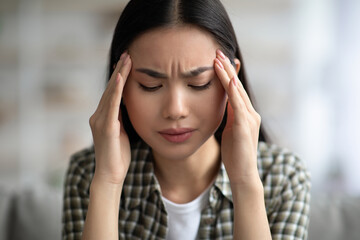 Closeup of young asian woman having headache, touching her temples