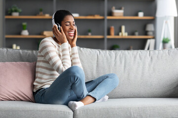 Obraz premium Domestic Pastime. Joyful African Female Listening Music In Wireless Headphones At Home