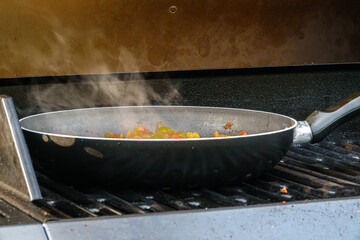 steam rising from the pan of food cooking outdoors over a BBQ grill