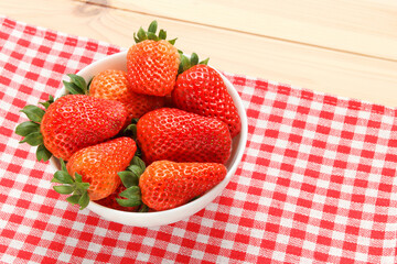 strawberries in the white ceramic bowl on the towel with wooden table background, rustic style