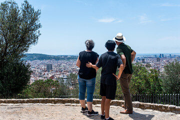 Obraz na płótnie Canvas Una familia de tres turistas contemplando las vistas de una ciudad en verano desde un mirador. Barcelona ciudad desde lo alto de una colina.