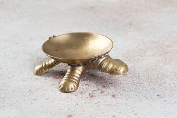 Old brass turtle ashtray on concrete background.
