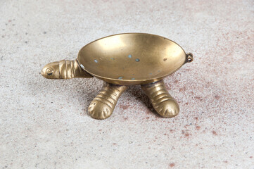 Old brass turtle ashtray on concrete background.