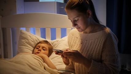 Young mother searching medicines for sick child on smartphone at night