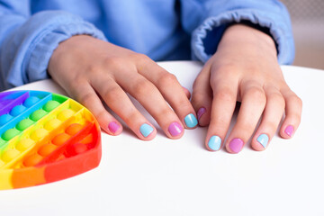 Little girl hands with beautiful manicure nails near toy, pop it