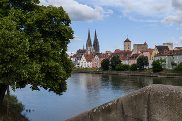 Obraz premium Blick von der Wöhrd auf Dom, steinerne Brücke , Rathausturm und Ufer mit Wolken am Himmel und Bäumen im Vordergrund