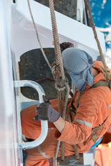 Seaman ship crew working aloft at height painting ships superstructure.