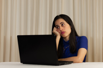 Woman sitting in front of her laptop. staring at the screen, bored, sleepy, tired. Latin woman in front of her laptop without spirits.