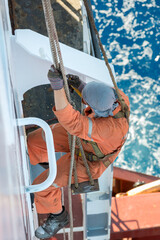 Seaman ship crew working aloft at height painting ships superstructure.