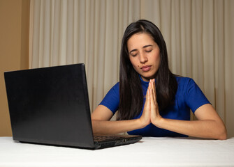 Christian and religious woman in front of the computer. virtual worship, virtual mass, virtual congregation. Woman praying in front of her laptop. faith. religious work.