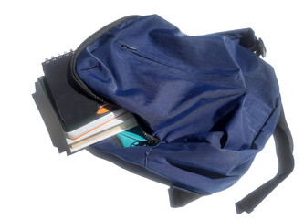 A blue backpack full of notebooks  and books on a white background 