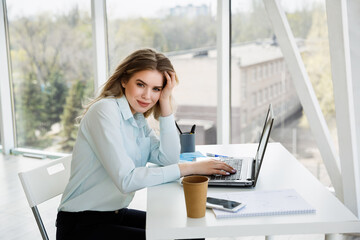 Young beautiful caucasian businesswoman or student works in the modern office with a laptop