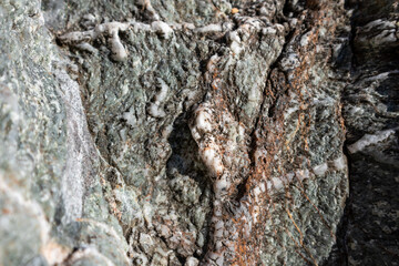 Wild big green marble rock with white and brown inclusions close-up texture. Various rocky surface on seashore in sunny Greece near Athens